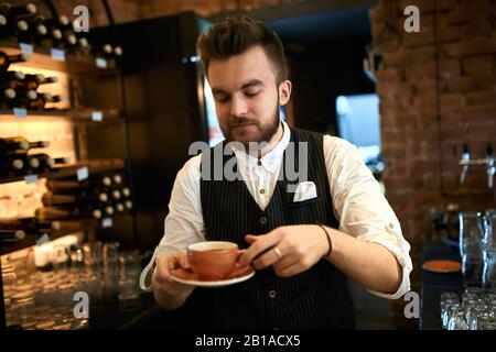 le jeune barista talentueux forme, enseigne aux clients en présentant et en expliquant le menu des boissons au café Banque D'Images