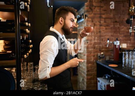 le jeune barista barbu conseille aux clients d'acheter, de boire, de goûter un nouveau café savoureux. gros plan sur la photo, souhaitez-vous du café Banque D'Images