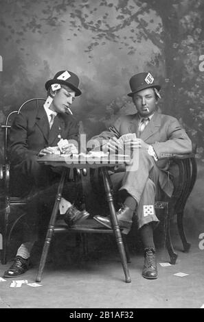 Deux jeunes hommes qui prétendent jouer aux cartes. Ils sont fumeurs et ils s'assoient près d'une petite table. Les deux hommes portent des chapeaux et ont leurs jambes croisées. Un homme est de peeking dans la main de carte de l'autre. Les deux gars ont des as, des rois et d'autres cartes visiblement "cachées" dans toutes les zones possibles sur eux-mêmes, ainsi que sur le sol. Aucun alcool n'est visible. Emplacement inconnu. Pour voir mes images vintage connexes, recherchez: Prestor vintage sport Banque D'Images