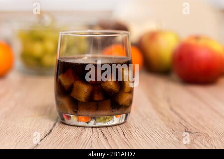 Un verre rempli de cubes de sucre et un verre de cola sont debout sur la table. À l'arrière-plan, les fruits, les pommes et les raisins de mandarine. Banque D'Images