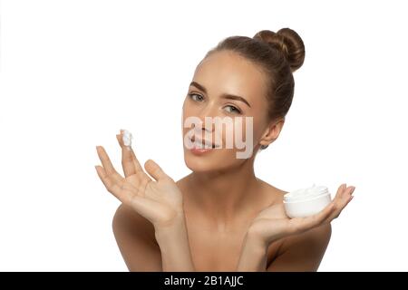 Belle jeune femme avec crème faciale dans ses mains isolée sur fond blanc. Banque D'Images