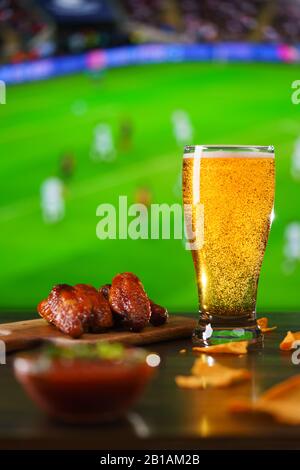 Ailes épicées de poulet barbecue, salsa de tomates, nachos et bière sur table de bar en bois sombre. Football sur fond, haute résolution Banque D'Images