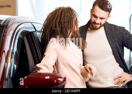 ypung attactive couple debout nexxt à rouge voiture et parler, penser à l'acheter ou pas. conversation. gros plan photo Banque D'Images