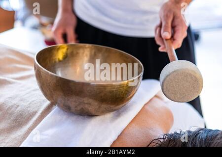 Un masseur debout avec un bol de son en bronze tibétain avec un bâton. Un massothérapeute professionnel offrant un massage sonore Banque D'Images