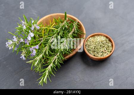 Brindilles violettes au romarin et au romarin frais dans un bol en bois d'olive et un petit bol de romarin entier séché sur fond d'ardoise noire Banque D'Images