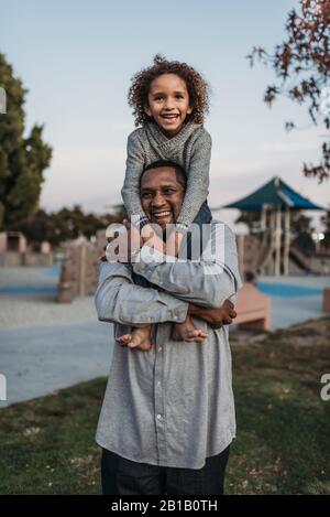 Fils joyeux assis sur les épaules d'un père heureux au terrain de jeu du parc Banque D'Images