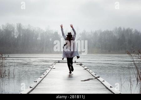 femme agitant ses mains dans l'air marchant le long d'une jetée à la plage Banque D'Images