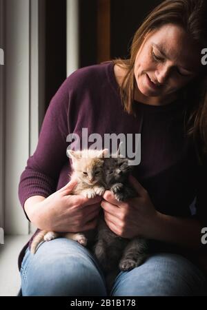 Femme regardant deux chatons adorables qu'elle tient sur ses genoux. Banque D'Images