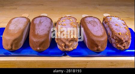 Les sucettes à glace enrobées de chocolat, se trouvant en rangée sur des blocs de congélation en plastique bleu, restent froides aussi longtemps que possible avant d'être mangées. Banque D'Images