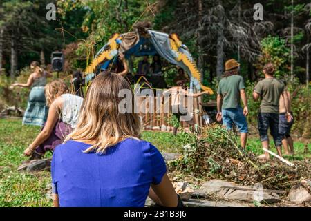 Un foyer sélectif tourné de derrière une dame blonde, se reposant sur un camping pendant un festival multiculturel de la terre, les gens flous sont vus danser en arrière-plan Banque D'Images