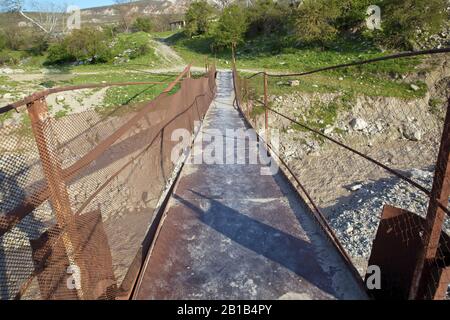 Une ancienne rivière rouillée étroite croisant . Sale, rivière pierreuse . un pont suspendu encore fait d'un support en fer a été utilisé pour traverser la rivière reliant le Banque D'Images