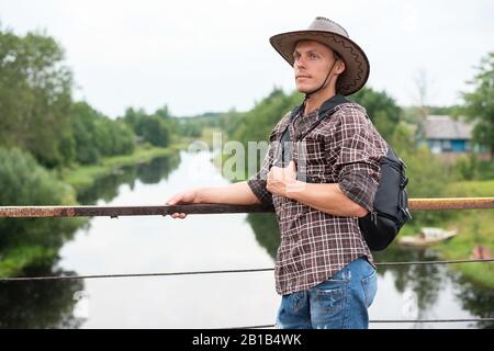 Un homme dans un chapeau de cowboy, avec un sac à dos sur le pont au-dessus de la rivière. Banque D'Images