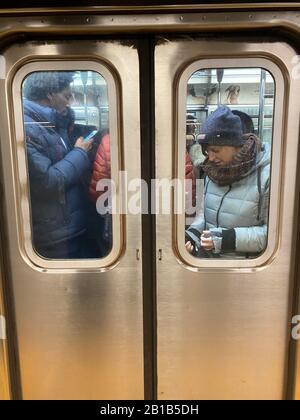 Les passagers du métro restent occupés sur leur téléphone portable pendant l'heure de pointe du matin toujours surpeuplée sur les trains allant de Brooklyn à Manhattan. Banque D'Images