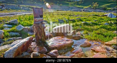 Tuyau de fer qui coule de l'eau potable propre . eau de source du sol Pierre rouge Colorfull . L'eau coule du tuyau contre la montagne floue Banque D'Images