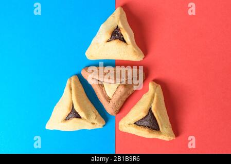 Concept de vacances Purim. Arrangement créatif de variété Hamantash sur fond de papier rouge et bleu. Les pâtisseries triangulaires de Hamantaschen ont également été appelées poches de Haman ou oreilles d'Oznei Haman-Haman. Banque D'Images