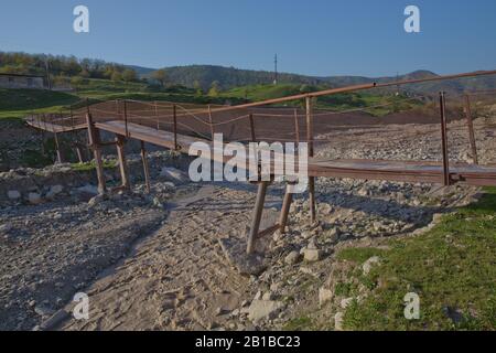 Une ancienne rivière rouillée étroite croisant . Sale, rivière pierreuse . un pont suspendu encore fait d'un support en fer a été utilisé pour traverser la rivière reliant le Banque D'Images