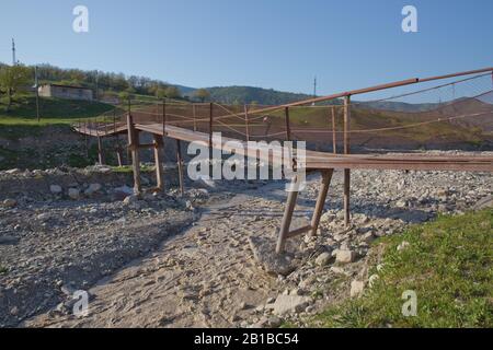 Une ancienne rivière rouillée étroite croisant . Sale, rivière pierreuse . un pont suspendu encore fait d'un support en fer a été utilisé pour traverser la rivière reliant le Banque D'Images