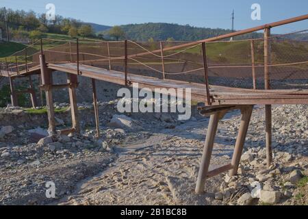 Une ancienne rivière rouillée étroite croisant . Sale, rivière pierreuse . un pont suspendu encore fait d'un support en fer a été utilisé pour traverser la rivière reliant le Banque D'Images