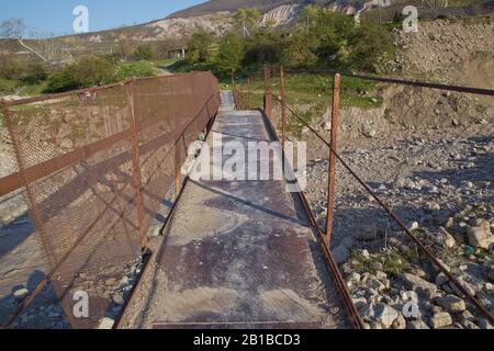 Une ancienne rivière rouillée étroite croisant . Sale, rivière pierreuse . un pont suspendu encore fait d'un support en fer a été utilisé pour traverser la rivière reliant le Banque D'Images