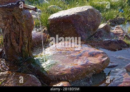 Tuyau de fer qui coule de l'eau potable propre . eau de source du sol Pierre rouge Colorfull . L'eau coule du tuyau contre la montagne floue Banque D'Images