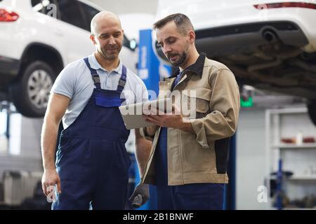 Taille vers le haut portrait de deux mécaniciens modernes de voiture utilisant une tablette numérique en se tenant dans la boutique automatique, espace de copie Banque D'Images