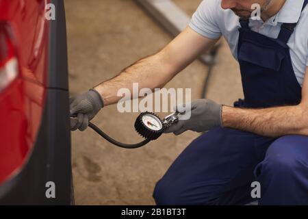 Gros plan du mécanicien de voiture vérifiant la pression dans les pneus lors de l'inspection du véhicule dans l'atelier de garage, espace de copie Banque D'Images