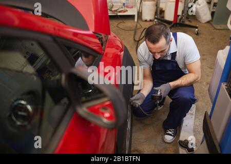 Vue en grand angle chez le mécanicien de voiture vérifiant la pression dans les pneus lors de l'inspection du véhicule dans l'atelier de garage, espace de copie Banque D'Images