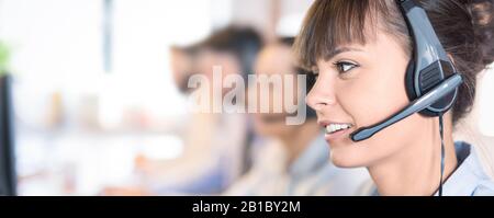 Travailleur de centre d'appel, accompagnée par son équipe. Smiling customer support au travail de l'opérateur. Jeune employé de travailler avec un casque. Banque D'Images