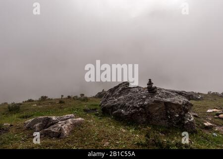 Une petite pyramide se trouve sur un grand bloc dans les montagnes avec un brouillard dense en arrière-plan. Météo sombre. Horizontal. Banque D'Images