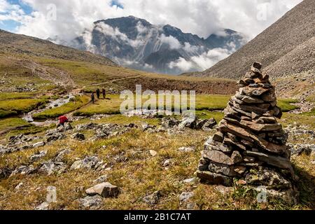 Un grand cairn au premier plan d'un paysage de montagne. Nuages blancs bas au-dessus des montagnes. Les touristes avec des sacs à dos vont le long du chemin Banque D'Images