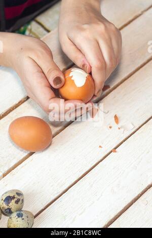 Les mains d'une femme non reconnaissable qui nettoie les œufs durs. Processus de nettoyage des œufs. Femme préparant le petit déjeuner. Nettoyage de l'oeuf de la coquille Banque D'Images