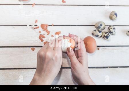 Les mains d'une femme non reconnaissable qui nettoie les œufs durs. Processus de nettoyage des œufs. Femme préparant le petit déjeuner. Nettoyage de l'oeuf de la coquille Banque D'Images