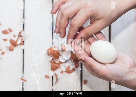 Les mains d'une femme non reconnaissable qui nettoie les œufs durs. Processus de nettoyage des œufs. Femme préparant le petit déjeuner. Nettoyage de l'oeuf de la coquille Banque D'Images