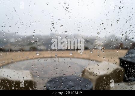 Vue de l'intérieur d'une maison au sommet d'une colline d'un patio et de la subdivision au-dessous de lorsque la pluie tombe. Prise par une fenêtre couverte de pluie et d'eau repérée . Banque D'Images