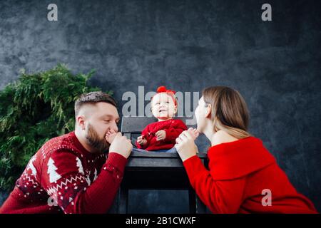 La famille en pull rouge embrasse les talons du bébé. Banque D'Images