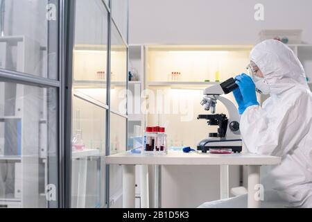 Vue latérale d'un médecin scientifique dans un masque de protection au microscope lors de l'étude de coronavirus dangereux en laboratoire Banque D'Images