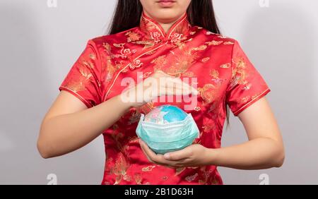 Une femme asiatique en costume chinois tenant le globe porter un masque hygiénique à la main pour prévenir les gestes. Maladie du monde de la situation d'éclosion de Coronavirus 2 Banque D'Images