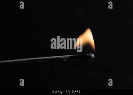 un match brûlant avec une flamme vive sur un fond noir Banque D'Images