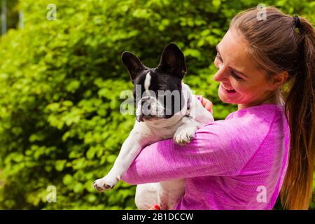 Amoureux des animaux, animaux domestiques, chiens fun concept. Happy smiling woman wearing clothes holding sport petit mignon bouledogue français à l'extérieur du parc Banque D'Images