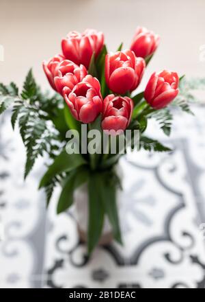 Vue rapprochée d'un bouquet de tulipes rouges dans un bol transparent au-dessus d'un sol hydraulique. Banque D'Images