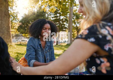 Portrait souriant d'une heureuse jeune femme afro-américaine assise avec ses amis dans le parc pour un pique-nique lors d'une chaude journée d'été Banque D'Images