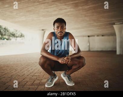 Portrait d'un coureur de fitness dans des vêtements de sport se croquant sur le pavé et regarde à l'appareil photo Banque D'Images