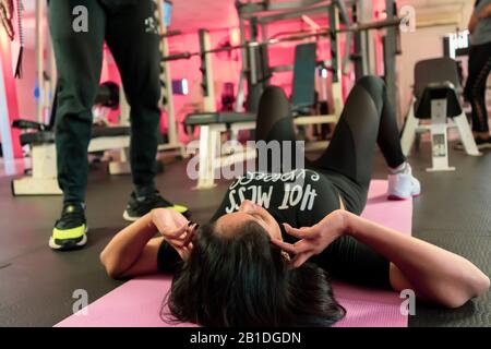 L'entraîneur aide la jeune femme à faire des exercices abdominaux sur le fond des balles de fitness. Belle femme faisant l'abs sur un tapis et un homme l'aide dans Banque D'Images