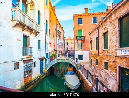 Un bateau isolé amarré le long d'un canal d'eau tranquille parmi de beaux bâtiments historiques peints colorés et des ponts de pied arqués à Venise, en Italie à l'aube avec Banque D'Images