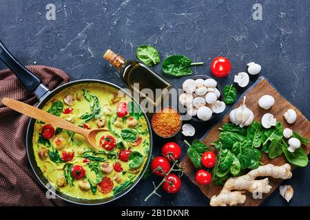 Curry végétarien sur une poêle de lait de coco aux champignons et légumes : épinards et tomates cerises sur fond de béton foncé avec ingrédient Banque D'Images