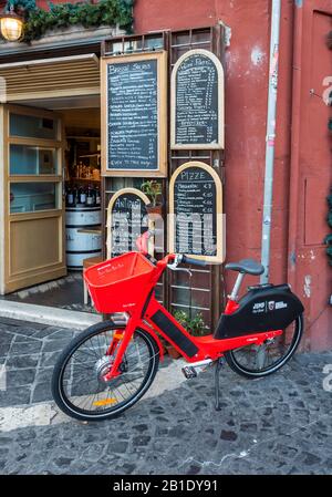 Location de vélos électriques AU VOLANT rouge à l'extérieur du restaurant italien avec menu de tableau noir manuscrit, Rome, Italie Banque D'Images