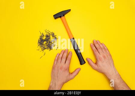 Marteau, mains mâles et pile de clous sur fond jaune Banque D'Images