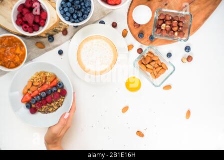 Vue de dessus montrant des mains mangeant des porridge avec des noix de miel, des bleuets sur la table blanche Banque D'Images
