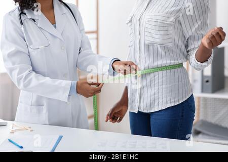 Femme afro nutritionniste mesurant la taille du patient en clinique Banque D'Images