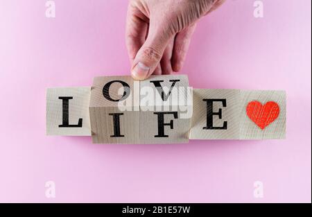 Blocs de jouets en bois tournant à la main avec des mots AMOUR VIE et coeur rouge symbole sur paquet rose Banque D'Images